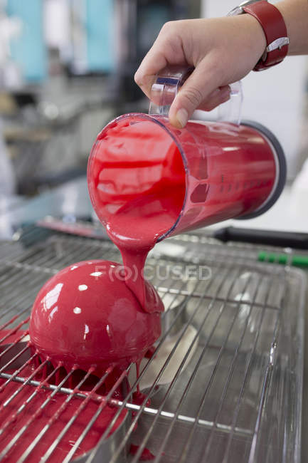 Abgeschnittene Ansicht des Chefs Hand gießt rote Glasur auf Kuchen — Stockfoto