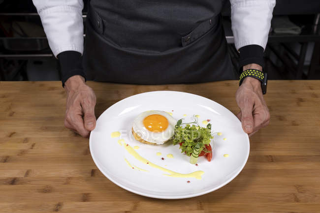 Cropped view of male chef holding plate with fried egg on toast — Stock Photo
