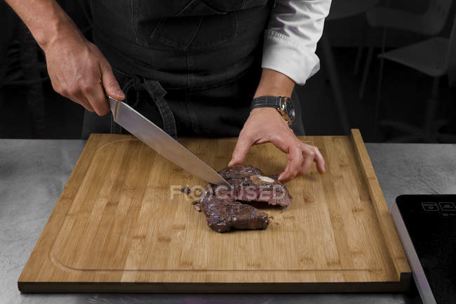 Cropped view of male chef cutting meat — Stock Photo