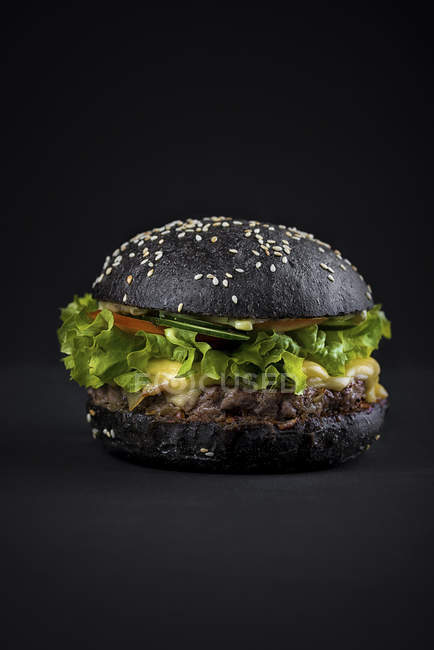Hambúrguer de carne em pão preto com folhas de salada verde — Fotografia de Stock