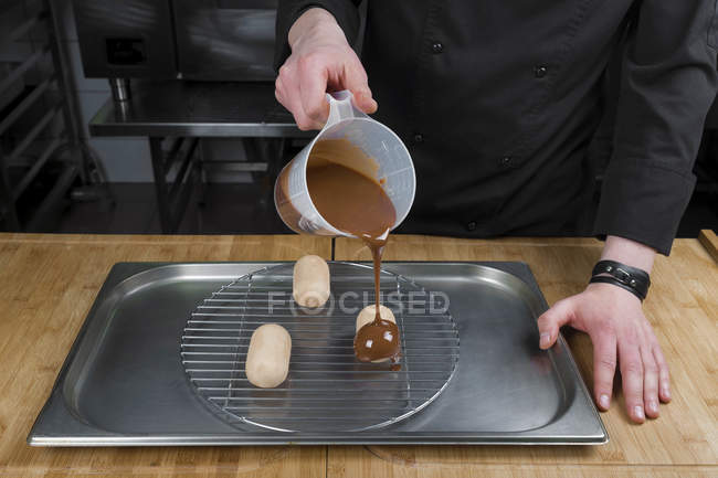 Vista cortada do chef derramando esmalte de chocolate em bolos — Fotografia de Stock