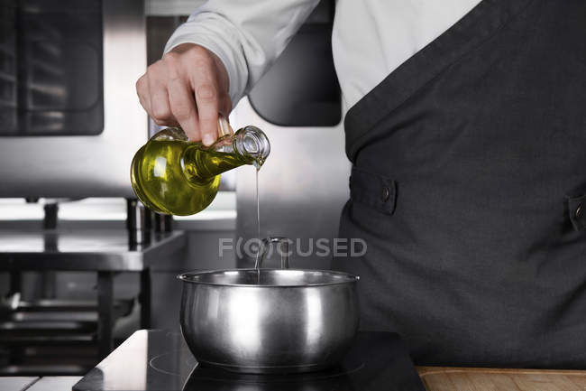 Vista recortada del chef masculino vertiendo aceite en la sartén - foto de stock