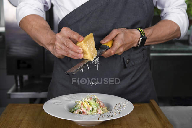 Cropped view of male chef grating cheese onto vegetable salad — Stock Photo