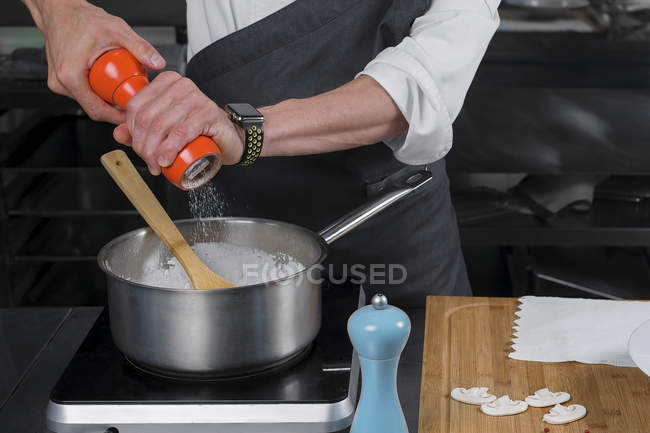 Cropped view of male chef salting cream of mushroom soup in pan — Stock Photo