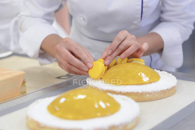 Female cook decorating cakes with yellow macarons — Stock Photo