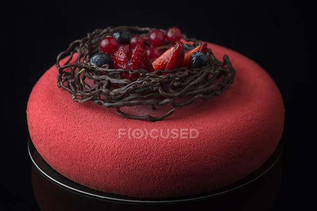 Cake with red icing and chocolate nest with fresh berries decoration — Stock Photo
