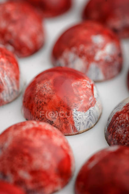 Doces de chocolate com esmalte de mármore vermelho, close-up — Fotografia de Stock