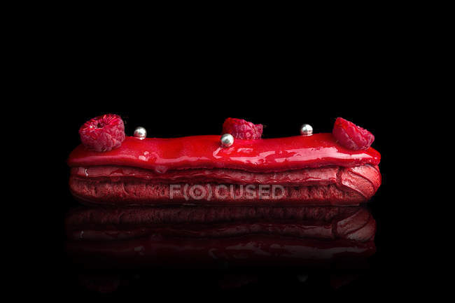 Eclair with red glaze and fresh raspberries — Stock Photo