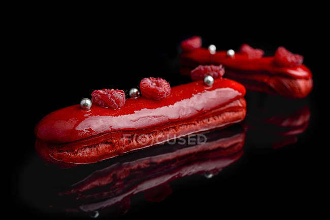 Eclairs con esmalte rojo y frambuesas frescas - foto de stock