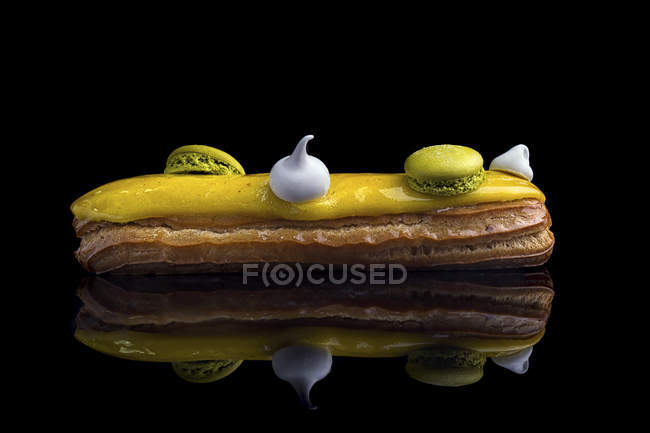 Eclair with yellow glaze and macarons decoration — Stock Photo