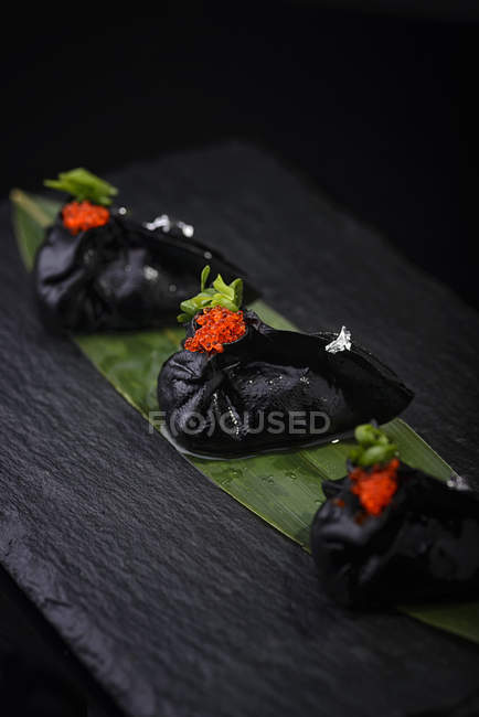 Черные пельмени с икрой на листе — стоковое фото