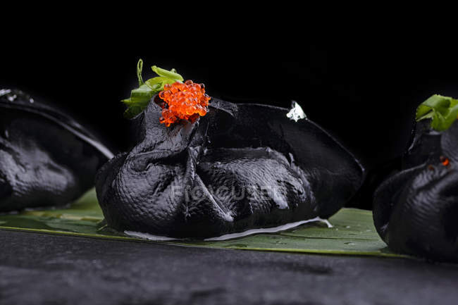 Чорні пельмені з ікрою, подані на листі, крупним планом — стокове фото