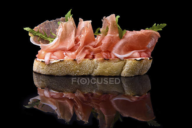 Bruschetta with prosciutto meat on black background — Stock Photo