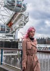 LONDRES, INGLATERRA - CIRCA ENERO, 2018: Mujer de pelo rosa caminando sobre terraplén frente al London Eye . - foto de stock