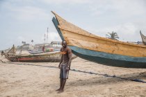 Чоловік, що стоїть поруч з причалюють човен на пляжі — стокове фото