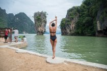 KHAO PHING KAN, THAILAND - CIRCA NOVEMBER, 16: Woman in swimwear stretching on coast with scenic view of limestone rocks. — Stock Photo