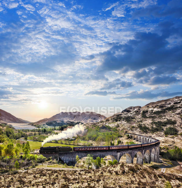 Glenfinnan Railway Viaduct in Scotland with the Jacobite steam train against sunset over lake — Stock Photo