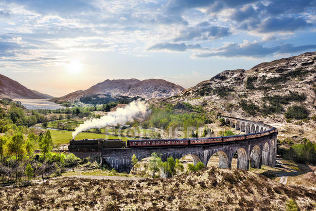 Glenfinnan Railway Viaduct in Scotland with the Jacobite steam train against sunset over lake — Stock Photo