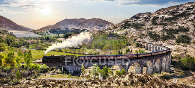 Glenfinnan Railway Viadotto in Scozia con il treno a vapore giacobita contro il tramonto sul lago — Foto stock