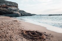 Песчаный замок на пляже со скалами в облачный день — стоковое фото