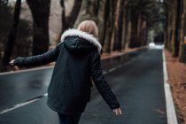 Vue arrière d'une jeune femme blonde marchant sur une route déserte en forêt — Photo de stock