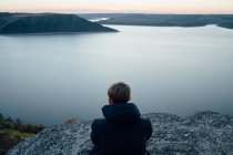 Молодой человек на вершине горы у спокойной реки — стоковое фото