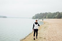 Elegante giovane uomo che parla con smartphone mentre cammina sulla spiaggia sabbiosa, vista posteriore — Foto stock