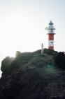 Віддалений вид на туриста, що стоїть на скелі на тлі маяка — стокове фото