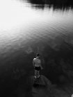 Visão traseira do homem em pé na rocha em meio ao rio no dia ensolarado — Fotografia de Stock