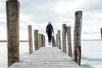 Blonde woman jumping at wooden pier over frozen lake — Stock Photo
