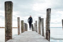 Blonde woman jumping on wooden pier at frozen lake — Stock Photo