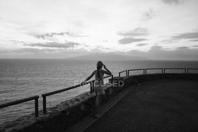 Вид сзади на девушку, идущую вдоль ручного перила над живописным морем — стоковое фото