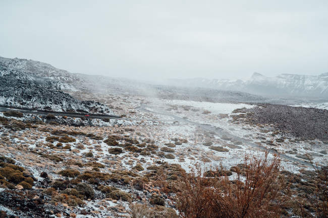 Vallée herbeuse couverte de neige, chaîne de montagnes sur fond — Photo de stock