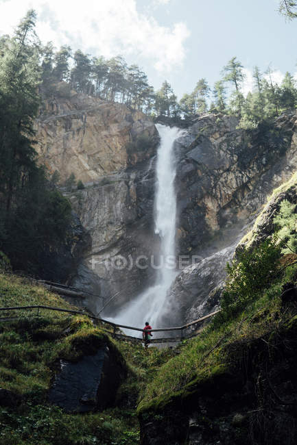 Vista à distância para a pessoa de pé na ponte sobre a cachoeira de rocha no fundo — Fotografia de Stock