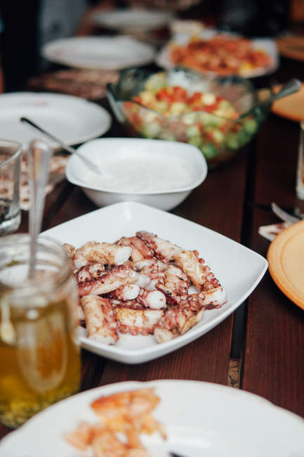 Керамическая тарелка с приготовленными щупальцами осьминога на деревянном столе — стоковое фото