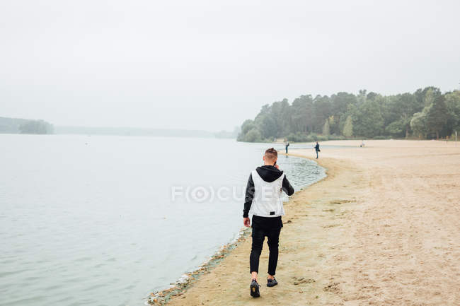 Stylish young man talking with smartphone while walking on sandy beach, rear view — Stock Photo