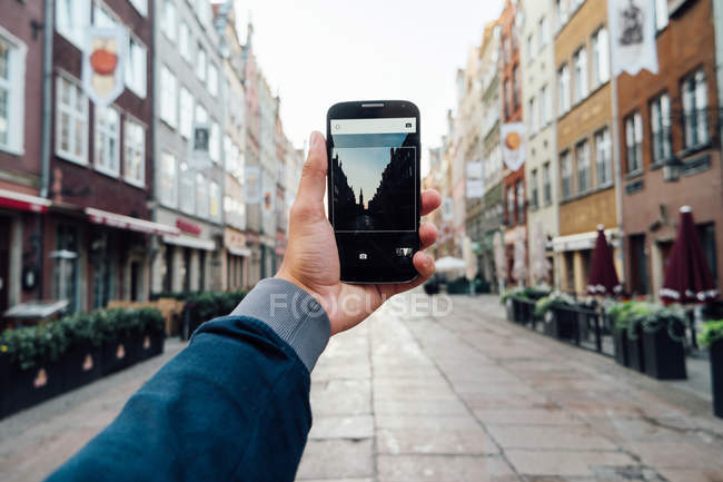 Maschio smartphone mano tenuta su sfondo paesaggio urbano offuscata — Foto stock