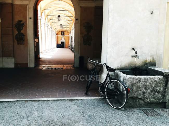 Bicicletta parcheggiata presso fontana pubblica sullo sfondo di edificio passaggio ad arco — Foto stock