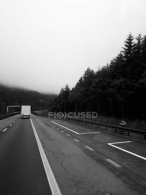 Camión en camino de asfalto corriendo a lo largo de terreno montañoso brumoso - foto de stock