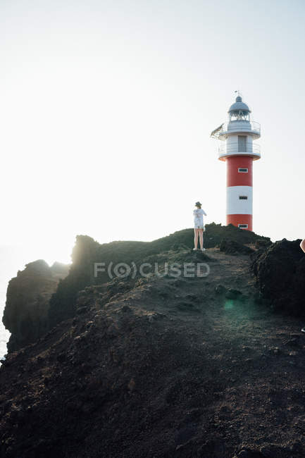 Vue lointaine du touriste debout sur la falaise sur le fond du phare — Photo de stock