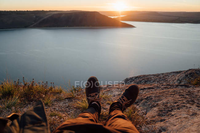 Sonnenbeschienene Beine von Touristen, die sich an der Küste des breiten Flusses ausruhen — Stockfoto