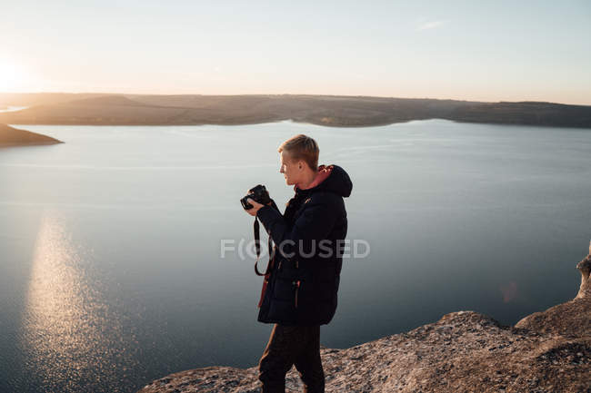Vista lateral de un joven fotógrafo tomando fotos de la naturaleza ribereña - foto de stock