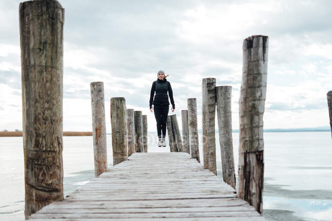 Donna bionda che salta al molo di legno sopra il lago ghiacciato — Foto stock