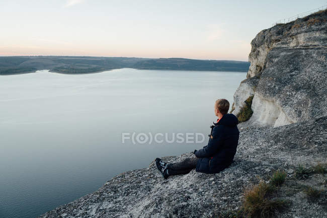 Вид сбоку на молодого человека, сидящего на берегу реки — стоковое фото