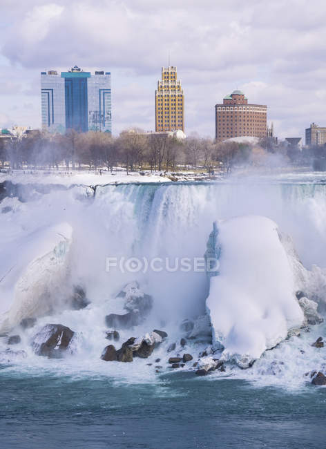 Niagara waterfall in winter time with buildings of city on background, Ontario, Canada — Stock Photo