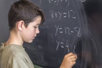 Schoolboy solving a problem on a blackboard. — Stock Photo