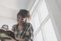 Молодая женщина в клетчатой рубашке с книгой и улыбкой — стоковое фото