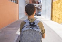 Вид сзади на школьника с рюкзаком прогуливающимся по городской улице днем — стоковое фото