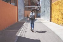 Вид сзади на школьника с рюкзаком прогуливающимся по городской улице днем — стоковое фото