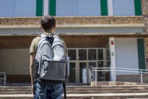 Вид ззаду на шкільного хлопчика, що стоїть і дивиться на будівлю школи — стокове фото